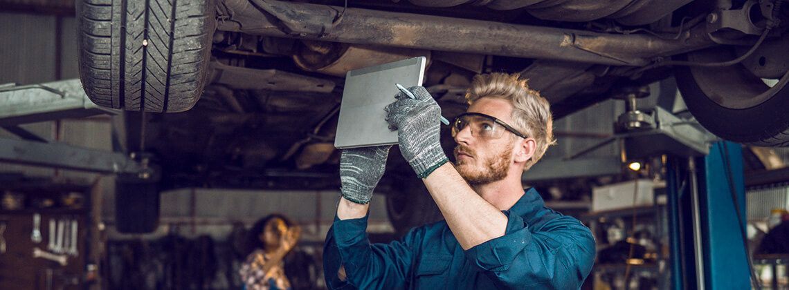 Ein junger Kfz-Mechatroniker mit Tablet in der Hand arbeitet an einem Auto.